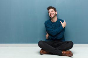 الشفاء في الوعي بالذات -A man practicing الشفاء while seated on the floor in front of a blue wall.