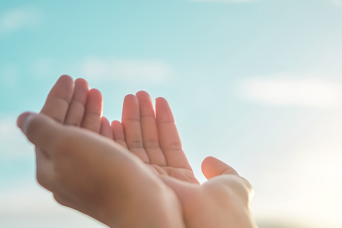 يقظة قبل فوات الأوان- A woman's hands are raised يقظة in front of a blue sky.