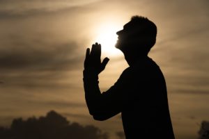 فوائد التوبة -A man in silhouette prays in front of the wide mercy gate.