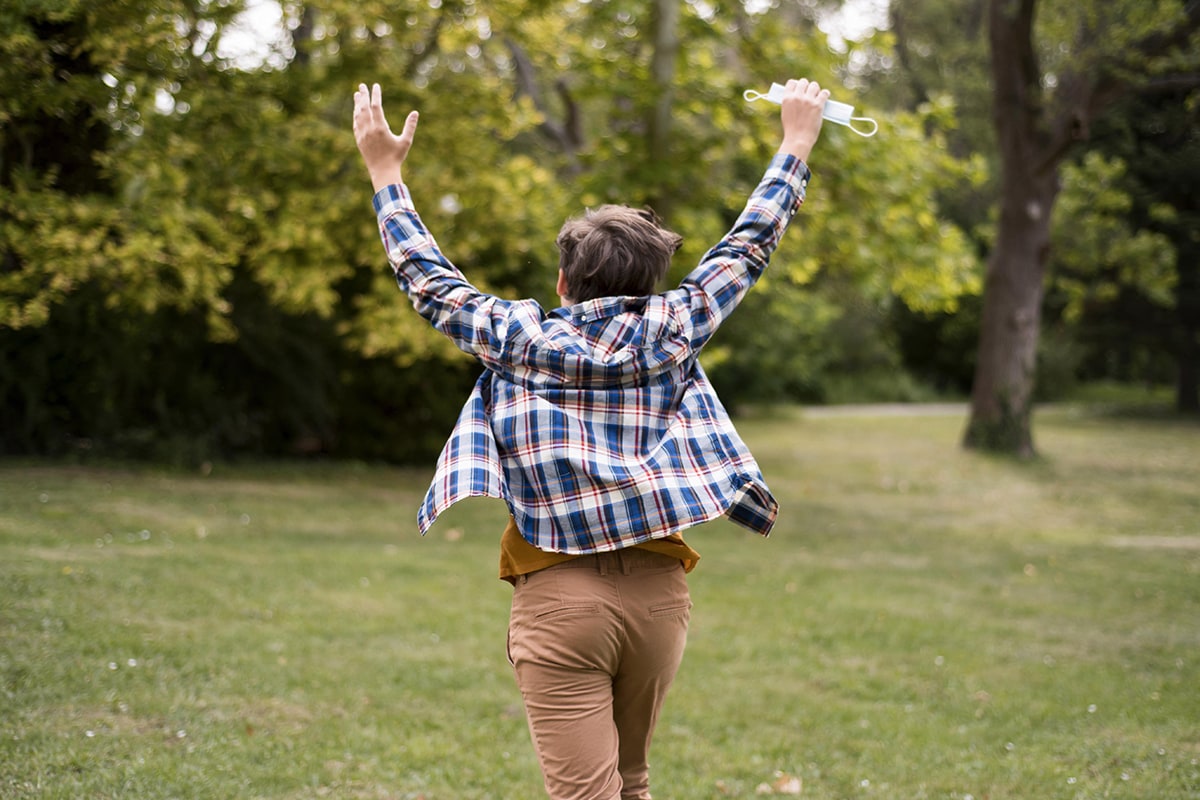 وسواس النظافة والطهارة : A boy in a park with his arms raised in the air, seeking أبواب الرحمة التوبة