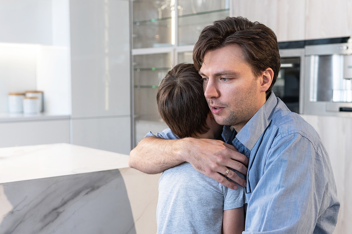 خوف شديد منذ الطفولة -A man is hugging his son tenderly in the kitchen, overcoming a deep fear since childhood.