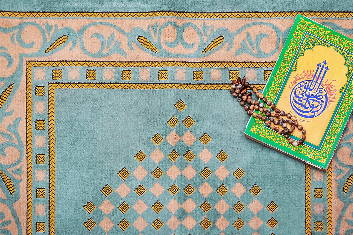 A blue rug adorned with a book and a rosary as symbols of victory over obsessive prayer.