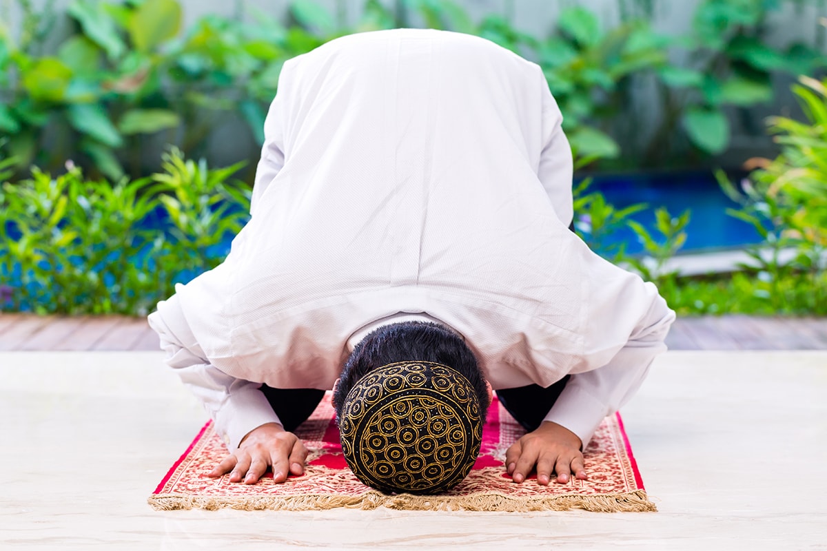 وسواس إعادة الصلاة- A man in a white shirt is finding solace through prayer on a rug.