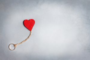 عدم الاقتران-A red heart symbolizing إشراق جديد, hanging from a rope in a contrasting gray backdrop after الجزع الأليم.