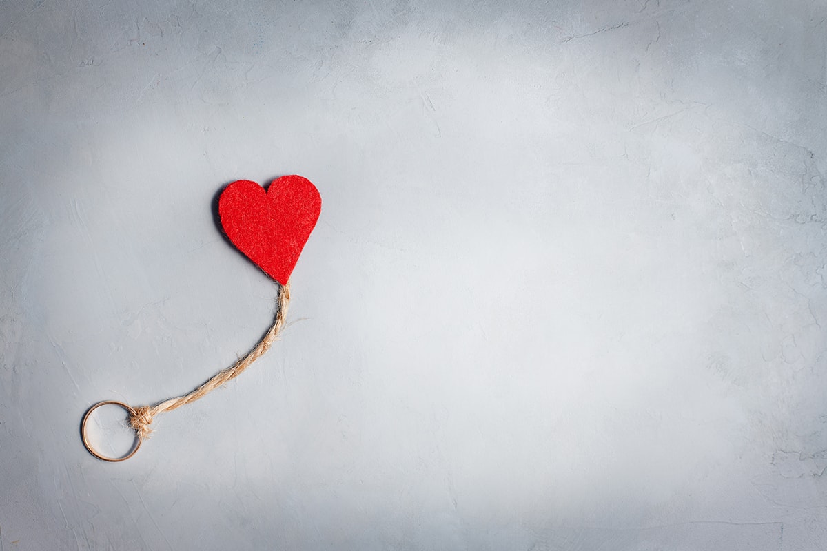 عدم الاقتران-A red heart symbolizing إشراق جديد, hanging from a rope in a contrasting gray backdrop after الجزع الأليم.