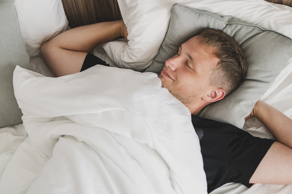 علاج الأرق - A man is sleeping calmly on a bed with white sheets, adhering to our cultural traditions.