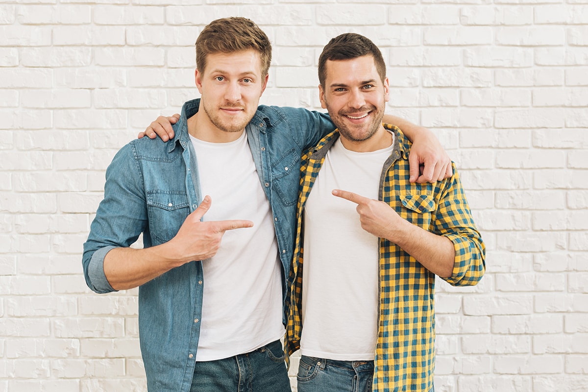 الصداقة لها حدود -Two determined men confidently pointing their fingers in front of a white brick wall, demonstrating the importance of perseverance and determination.