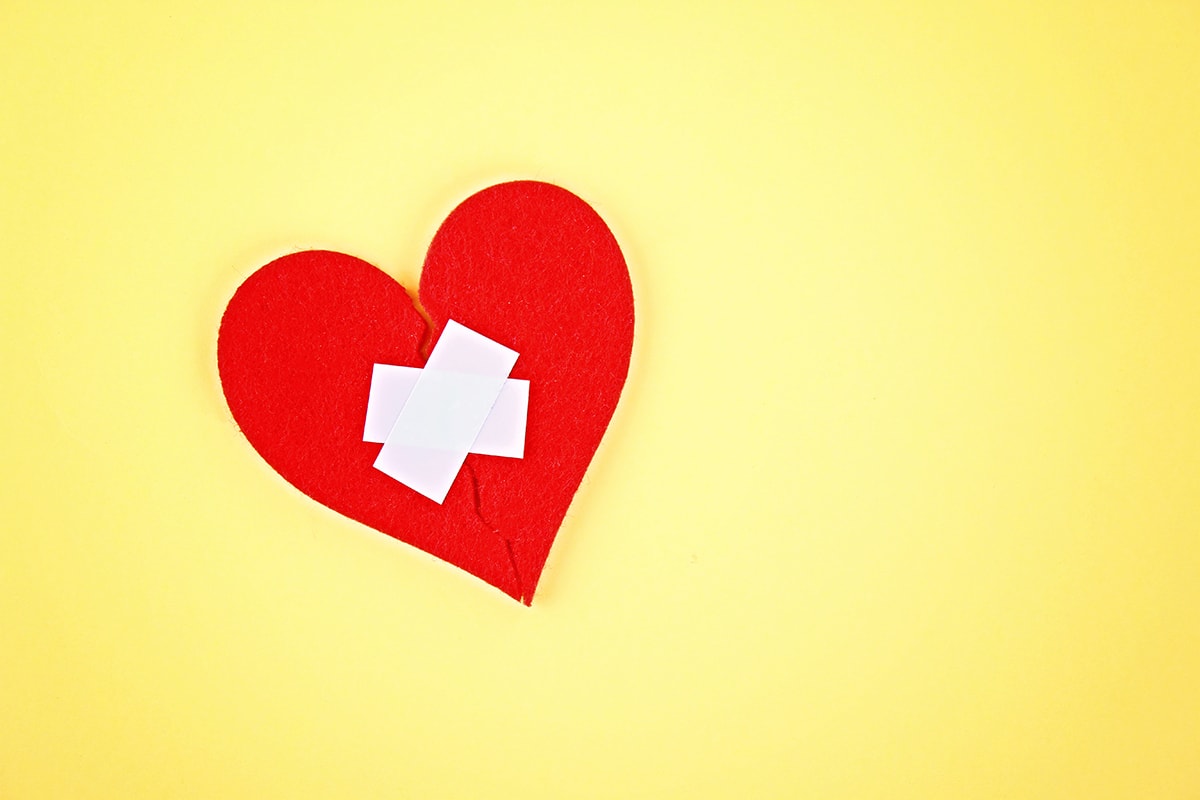 قصة عن الطلاق -A red heart with a bandage on it, resiliently overcoming germ obsession on a yellow background.