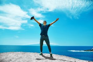 A man is standing on top of a cliff, قام متعافيًا من الوسواس الفكري, with his arms outstretched.